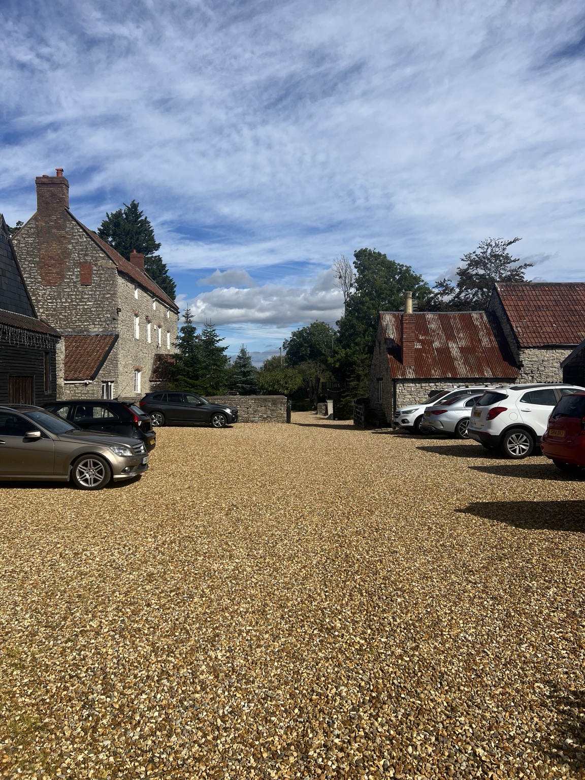 Cars parked in the spacious gravel courtyard by the stone farmhouse